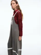 Mono largo de color negro con corte holgado y perneras anchas. Presenta detalles de encaje blanco y tela estampada floral en los tirantes, el bolsillo frontal, la parte inferior de las piernas y el ruedo.