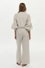 Camisa de lino color beige, con escote en V, cuello mao y mangas abullonadas tres cuartos. Cuenta con cierre frontal de botones y tiras ajustables para atar en la cintura.