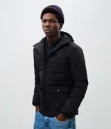 Campera tipo puffer de hombre, color negro, con capucha ajustable, cierre frontal por cremallera y bolsillos cargo frontales con solapa. Confeccionada en poliéster con diseño acolchado.