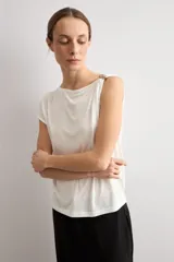 Blusa blanca de manga corta y corte recto, con escote bote y detalle metálico circular en el hombro.