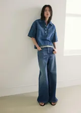 Jeans de denim azul de tiro medio y diseño wide leg largo, con cinco bolsillos, trabillas para cinto y cierre de botón y cremallera.