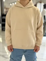 Canguro oversize de color beige con capucha, bolsillo frontal tipo canguro y puños y dobladillo en rib.