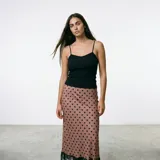 Falda midi de corte al bies, color beige con estampado de lunares negros. Presenta un detalle de encaje negro en el ruedo.