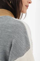 Cárdigan tejido de punto grueso, con diseño color block en gris, blanco y beige. Tiene cuello en V, cierre frontal con botones y un bolsillo de parche.