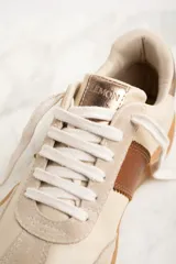 Zapatillas bajas color crema con puntera de gamuza beige, detalle de franja lateral en cuero marrón y contrafuerte en cuero metalizado color cobre.