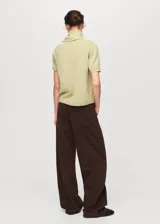 Jersey de punto fino color verde claro, con cuello redondo y manga corta. Presenta un diseño recto y un detalle de pañuelo integrado en el cuello.