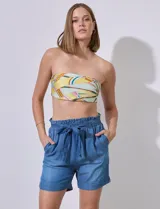 Short de tencel color azul medio, tiro alto, con pretina ancha elastizada y lazo de ajuste. Presenta bolsillos verticales delanteros y dobladillo en la pierna.