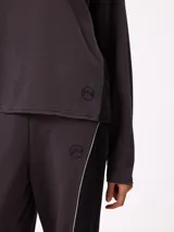Sweater de corte oversize y estilo cropped, color gris oscuro, con cuello redondo y detalle de costura en forma de X en el pecho. Presenta un pequeño logo bordado en el ruedo inferior.