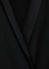 Vestido corto de color negro con diseño cruzado, cuello en pico con solapa tipo blazer y manga larga. Presenta un lazo en la cintura que permite ajustar la prenda y un tejido fluido y ligero con forro interior.