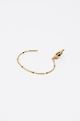 Pulsera rígida dorada con dije circular central que presenta un calado en forma de corazón y borde de esmalte negro con letras. Incluye cierre de gancho y detalles decorativos en color negro.