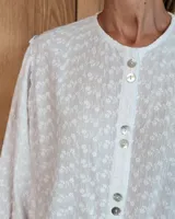 Camisa de manga larga con diseño de rayas verticales y bordados sutiles. Presenta cuello redondo, cierre frontal con botones y mangas abullonadas con volados en los hombros.