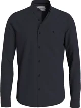 Camisa de manga larga color azul marino oscuro, de corte slim, confeccionada en algodón elástico mercerizado. Presenta cuello en punta, puños segados, bajo redondeado y un pequeño logo bordado de Calvin Klein en el pecho.