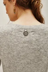 Sweater de punto color gris melange, con cuello redondo, manga larga y detalle de volado en el ruedo. Presenta pequeñas aplicaciones de strass distribuidas por toda la prenda.