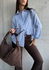 Camisa celeste de manga larga con cuello clásico, botones frontales y bordados florales en el pecho.