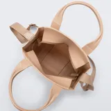 Cartera tipo tote bag Melissa modelo Mini Dulce, color beige con acabado brillante. Está fabricada en Melflex, un material de PVC flexible, e incluye asas de mano fijas y una correa ajustable y extraíble de tela con el nombre de la marca grabado.