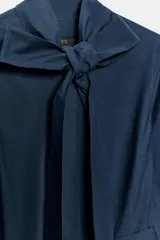 Vestido midi de algodón con cuello con lazada, manga tres cuartos y falda evasé. Incluye cinturón ajustable del mismo tejido y cierre frontal con botones.