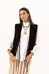 Chaleco oversize confeccionado en cuero descarne, con diseño de terminación en picos. Presenta lazos frontales con ojalillos metálicos y detalle de tachas metálicas en hombros y espalda.