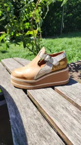 Zapatos tipo guillermina de cuero con plataforma y suela chunky de goma. Combinan tonos tostado liso, detalles metalizados y textura reptil en la parte trasera, con tira y hebilla de ajuste en el empeine.