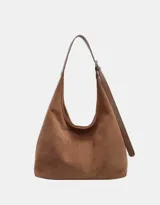 Bolso tipo hobo de material tipo gamuza o nobuk, color marrón camel. Presenta un diseño de silueta suave y caída, con una correa de hombro delgada de cuero liso del mismo tono.