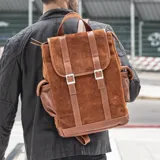 Mochila de cuero marrón con tapa y doble hebilla frontal, bolsillo trasero con cierre y bolsillos laterales con broche a presión. Interior forrado con bolsillo con cierre y bolsillo para celular.