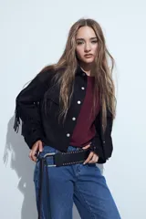 Campera negra de estilo western con flecos en las mangas, corte cropped, bolsillos frontales y cierre con botones metálicos.