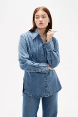 Camisa de jean negro con diseño de frunces verticales en el frente, cuello clásico, cierre frontal con botones y mangas largas con puños abotonados.