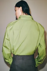 Camisa oversize de popelín de algodón color verde claro, con cuello solapa y manga larga. Cierre frontal con botones ocultos y bajo redondeado.