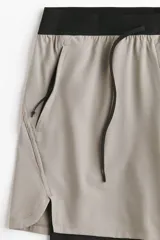 Short deportivo de doble capa color gris claro, con cintura elástica negra, cordón de ajuste y calza interna incorporada.