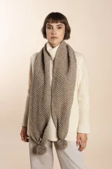 Bufanda tejida a mano en punto arroz, color marrón claro, con terminaciones de pompones en los extremos.