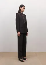 Blazer de corte sastre y diseño cruzado, con cierre de botones frontales, solapas clásicas y bolsillos laterales con solapa. Presenta una estructura entallada y hombros definidos.