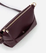 Bolso bandolera pequeño color borgoña, confeccionado en poliuretano con detalle texturizado tejido en la parte inferior. Cuenta con correa transversal ajustable, cierre de cremallera y bolsillo frontal con botón.