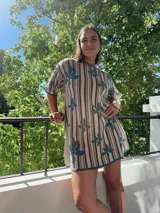 Vestido tejido de hilo de algodón con diseño de rayas verticales en tonos beige, marrón y verde, y estampado de hojas verdes. Tiene manga corta, cuello redondo y silueta holgada.