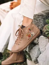 Botín de cuero serraje color beige, con cordones y detalle de flores bordadas en el lateral. Cuenta con suela plana de goma y cierre de cremallera lateral.