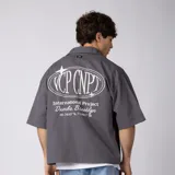 Camisa de manga corta color marfil, corte boxy, con cuello camisero, cierre frontal de botones y pequeño bordado marrón en el pecho con las siglas VCP.