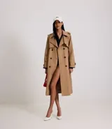 Trench coat largo de Marfinno, confeccionado en gabardina de poliéster. Presenta cuello con solapas, aletas en los hombros, cierre frontal con botones y cinta para lazo en la cintura.