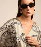 Blusa de tela satinada color gris con estampado abstracto en negro y blanco, escote en V cruzado, mangas cortas y cintura elastizada.