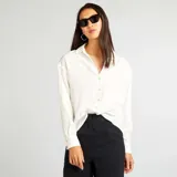 Camisa blanca de corte holgado con cuello clásico y mangas largas.