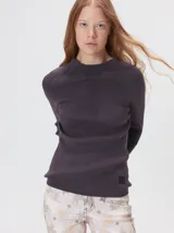 Remera de cuello alto tipo polera, confeccionada en tela rib con textura acanalada y ajuste al cuerpo. Presenta mangas largas y un pequeño bordado distintivo en la parte inferior.