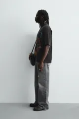 Camiseta de punto negro con efecto lavado, corte relaxed fit y cuello redondo. Presenta un estampado frontal con tipografía gótica en azul y una imagen circular que simula un iris en tonos rojizos y amarillos.