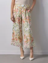 Pantalón capri de lino color crudo con estampado de hojas en tonos verdes, amarillos y naranjas. Presenta bolsillos laterales y detalle de puntilla en el ruedo.