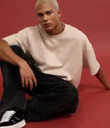 Remera oversized color beige confeccionada en gamuza sintética. Presenta cuello redondo, mangas cortas y bordado de cruz en el frente.