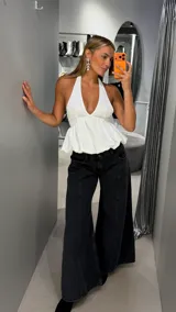 Top blanco con escote halter profundo y diseño peplum fluido, con corte ajustado en el busto y vuelo inferior.