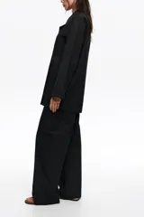 Pantalón tobillero de corte barrel color negro, con cierre frontal de corchete oculto y cremallera, tiro medio, bolsillos delanteros en costura y bolsillos traseros tipo plastrón. Presenta pespuntes a contraste.