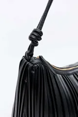 Bolso tipo hobo Daniel Cassin modelo Bolden, color negro, con diseño plisado y asa de hombro con nudos decorativos en los extremos.