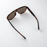 Lentes de sol tipo escudo con armazón de policarbonato marrón oscuro y detalles metálicos dorados en las patillas, con cristales degradados en tonos marrones y protección UV400.