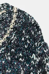 Jersey de punto con mezcla de hilos en tonos oscuros, blancos y azules, con escote en pico y manga larga. Presenta detalles de líneas en color crema en el cuello, puños y ruedo.