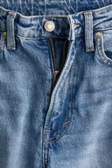 Jeans de cinco bolsillos en denim de algodón con leve stretch, tiro alto y cierre de botón. Corte ajustado de cintura a muslo, y pierna ancha (bootcut) desde la rodilla hasta el bajo. Presenta un lavado celeste medio con efecto desgastado.