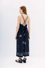 Vestido midi de viscosa con estampado floral sobre fondo azul oscuro. Presenta escote delantero, breteles finos que se cruzan en la espalda y cintura con lazo ajustable.