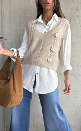 Chaleco de punto color beige con escote en V, diseño de trenzas verticales y tres flores tejidas en relieve.