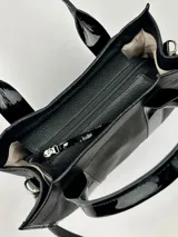 Bolso tote negro de cuero con detalles de charol, doble asa corta y correa bandolera de tela con letras.
